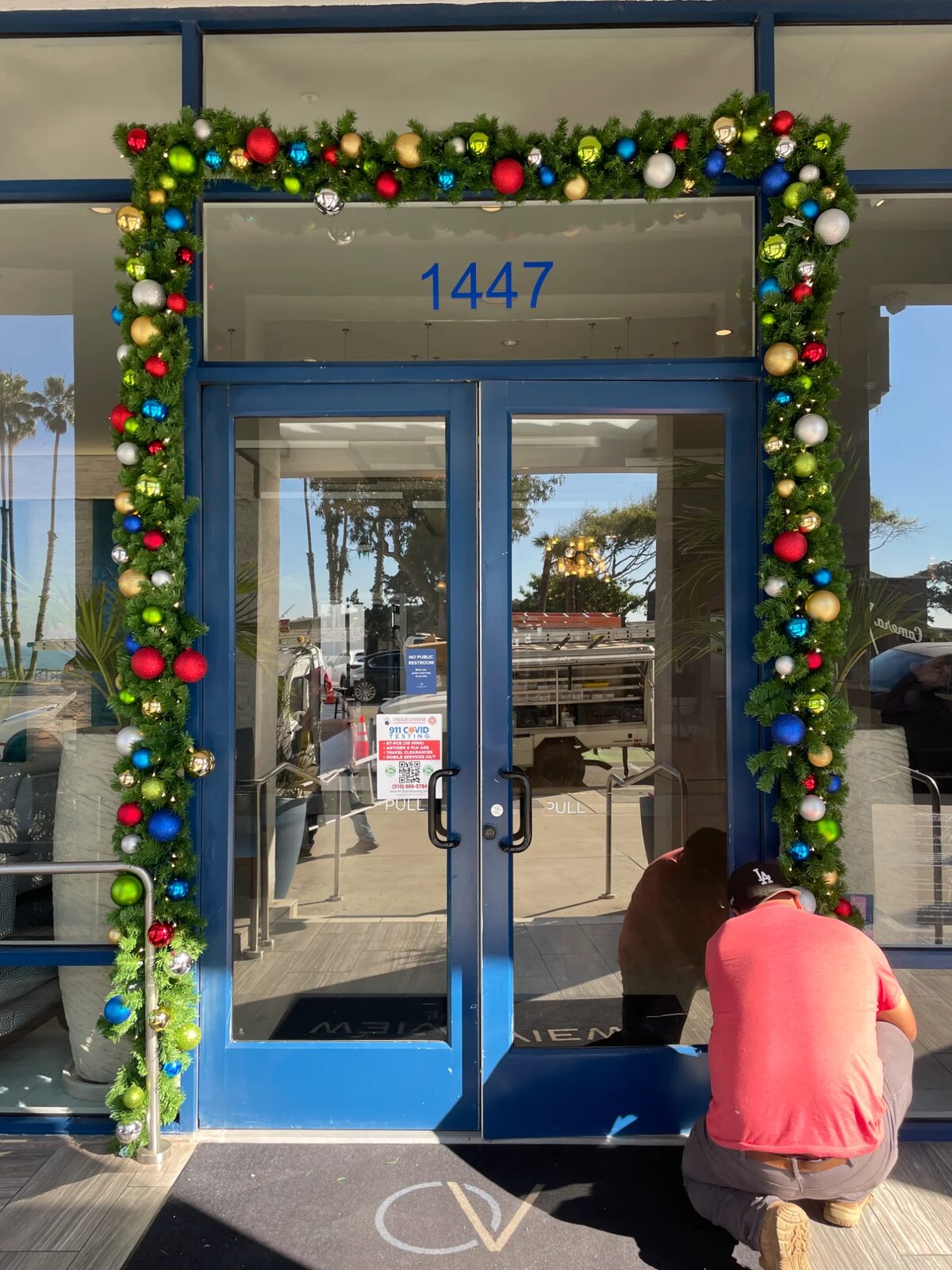 Crew member installing garland and ornaments around a glass entrance