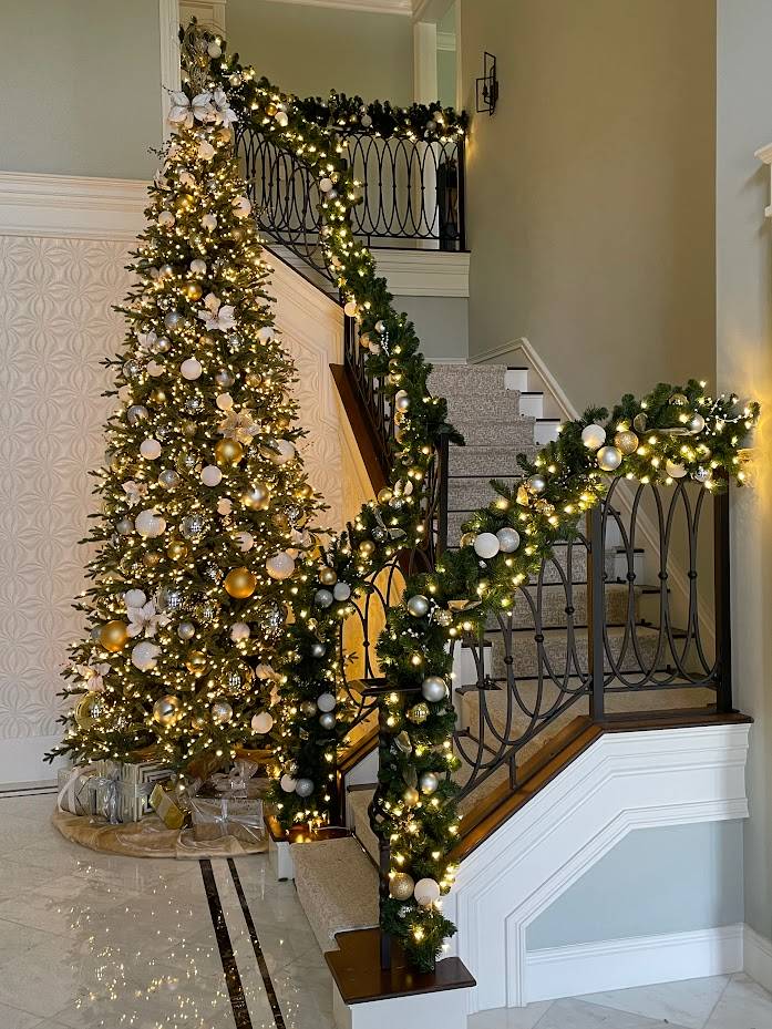 Decorated Christmas tree beside a garland-wrapped staircase