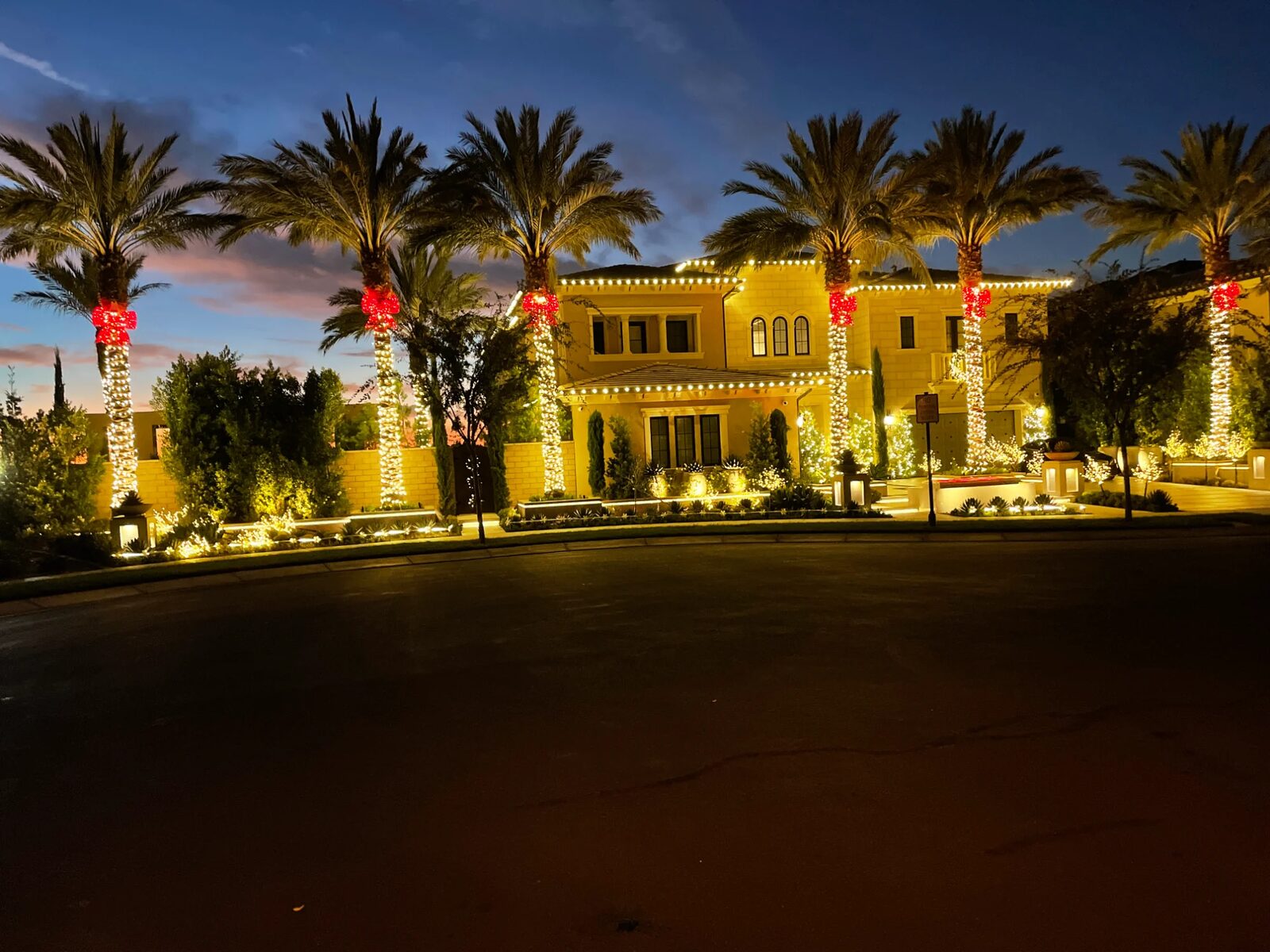 Mediterranean home with palm trees wrapped in warm white lights and red bows