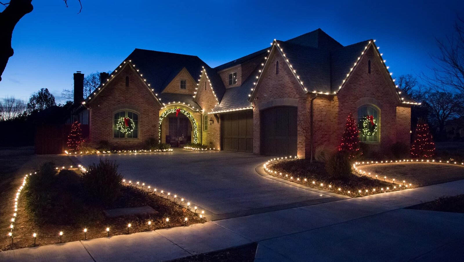 Brick home with warm white gables and lit walkway borders